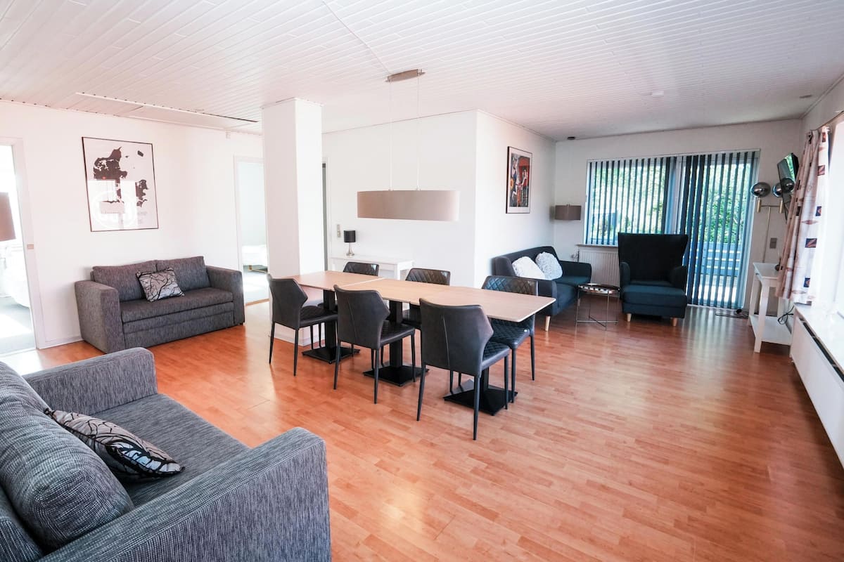 Una sala de estar moderna con comedor, piso de madera y un gran ventanal con persianas.