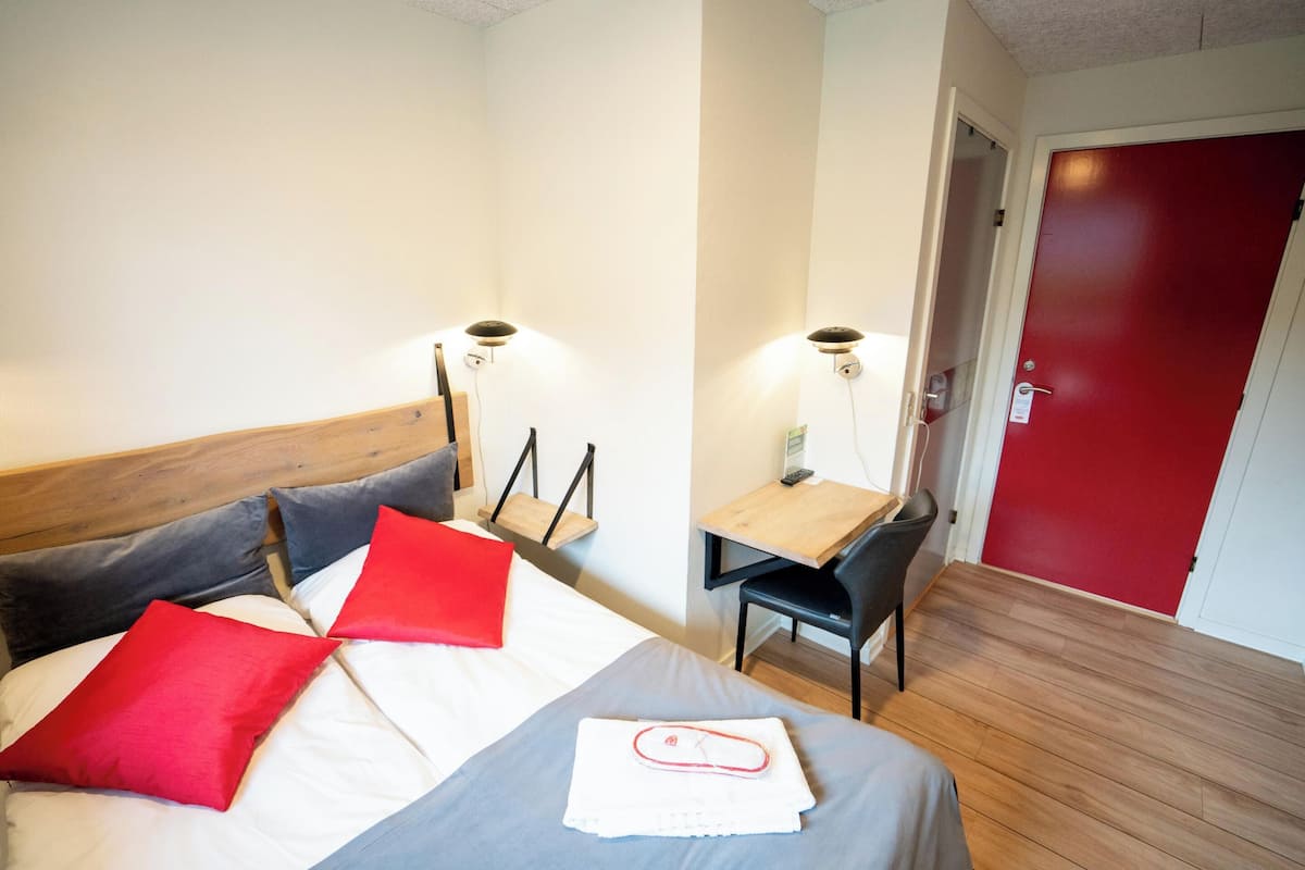 Una habitación de hotel con cama, escritorio, silla y una puerta roja.
