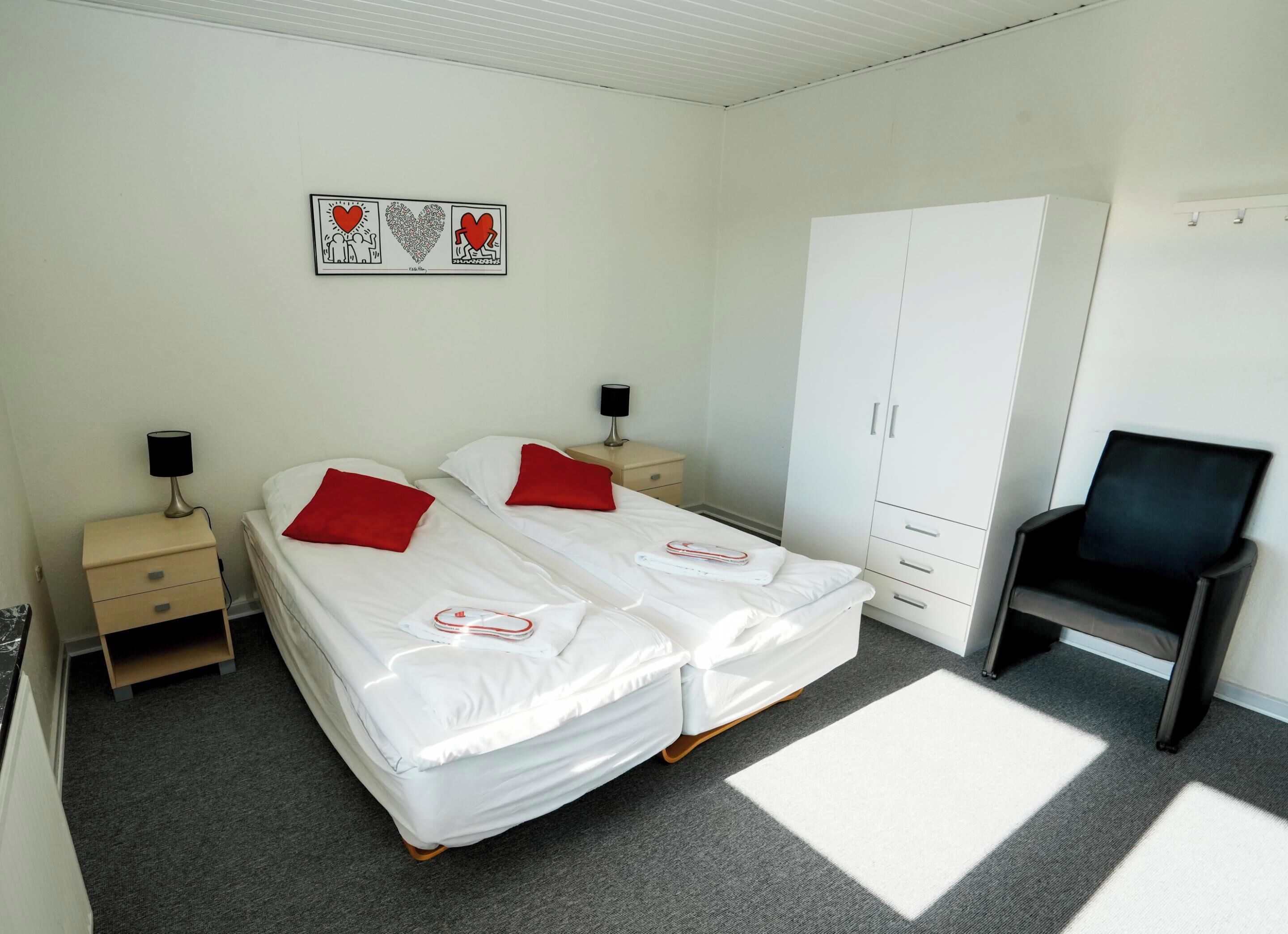 Un dormitorio con dos camas individuales, un armario, una silla y una obra de arte en la pared.
