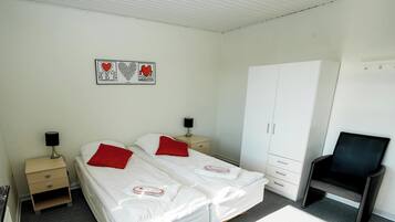 Un dormitorio con dos camas individuales, un armario, una silla y una obra de arte en la pared.