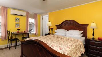 A bedroom with a wooden bed, a bedside table with lamps, a chair, a desk, and a window with curtains.