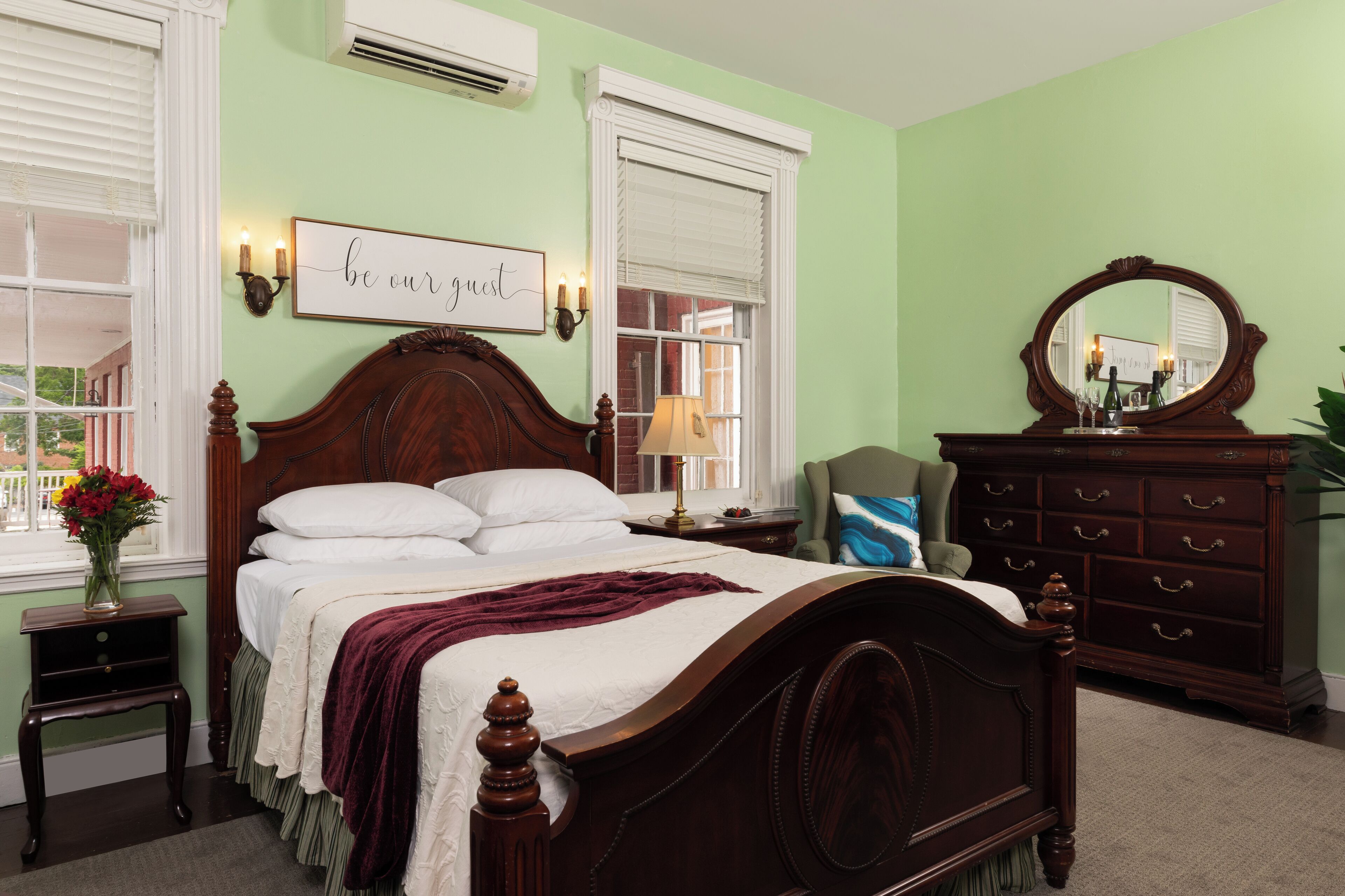 A bedroom with a large bed, a dresser, a mirror, and a bedside table with a lamp.