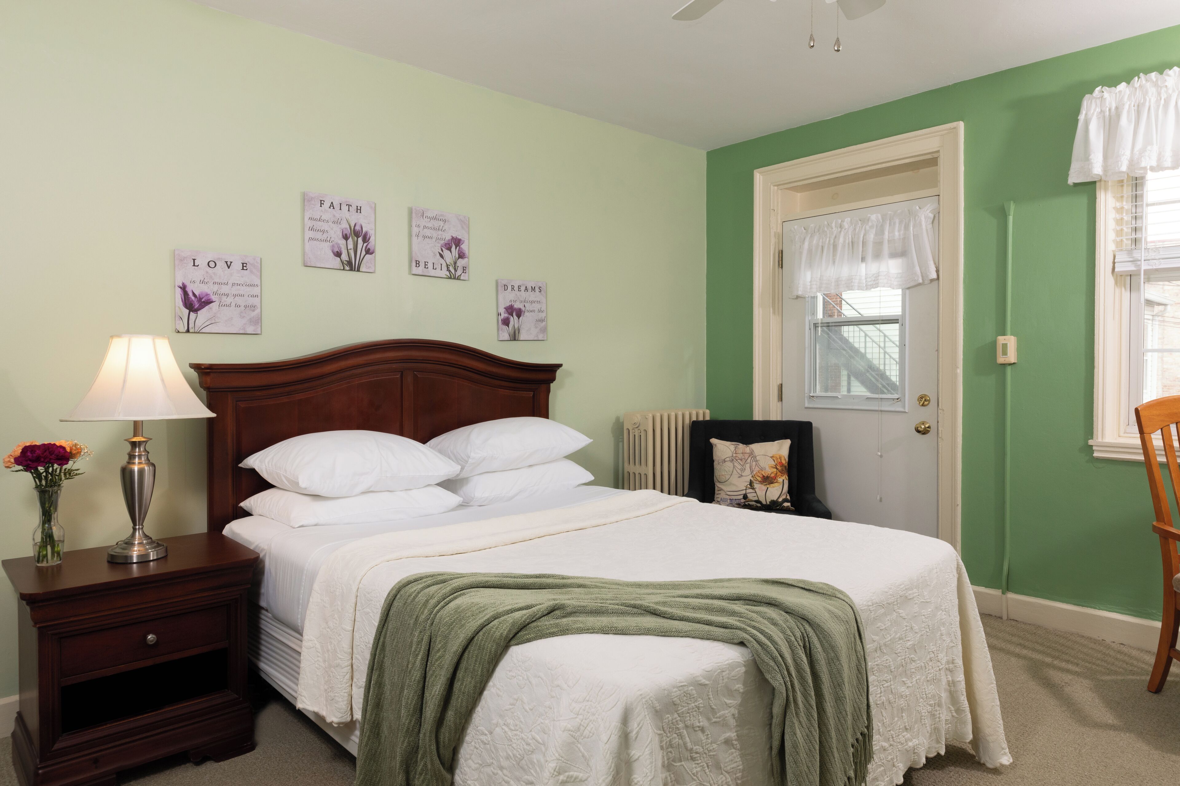 Quarto com cama, mesa de cabeceira, abajur e decoração na parede.