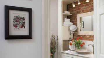 A bathroom with a white vanity, a mirror, a sink, and a brick wall. There are framed pictures on the wall and a vase with flowers on the counter.