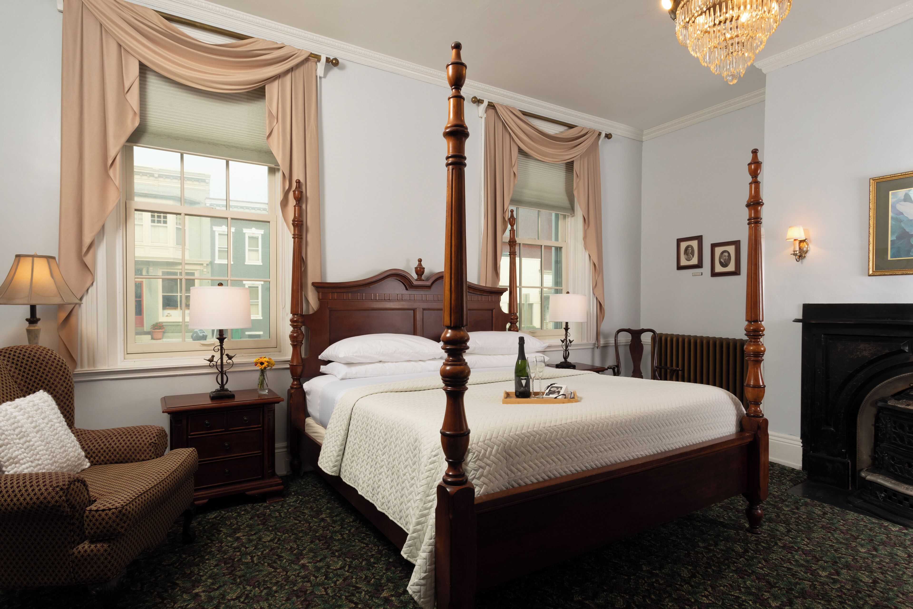 A four-poster bed with a wooden frame, a bedside table with a lamp, a chair, and a fireplace.