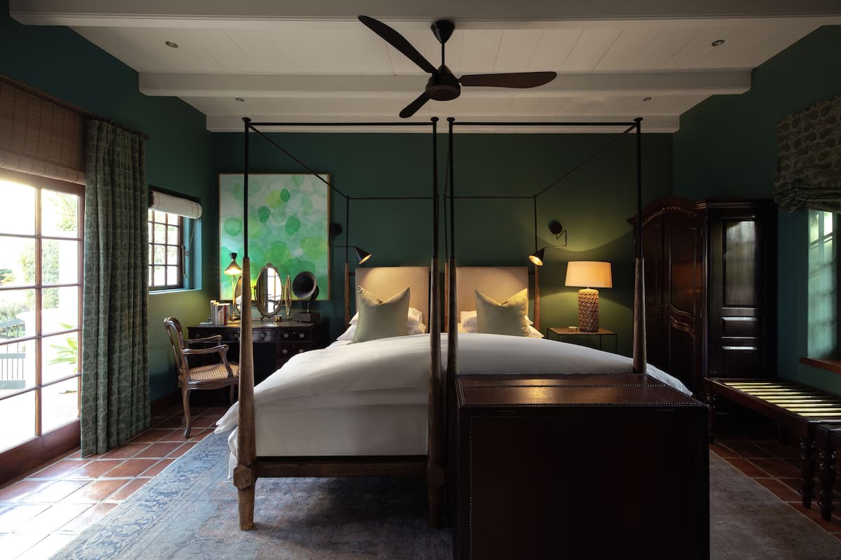 Un lit à baldaquin, un bureau avec une chaise, une lampe et un grand miroir au mur.