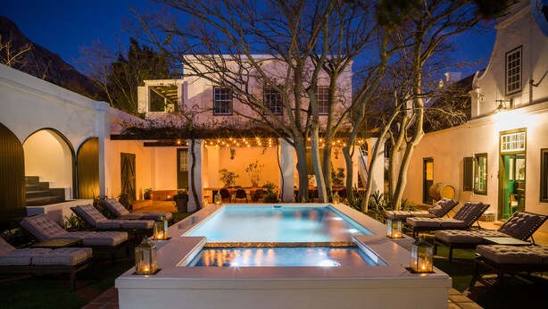 Un espace piscine doté de chaises longues et d’un jacuzzi, entouré d’un bâtiment blanc avec des portes en arc de cercle et un escalier.