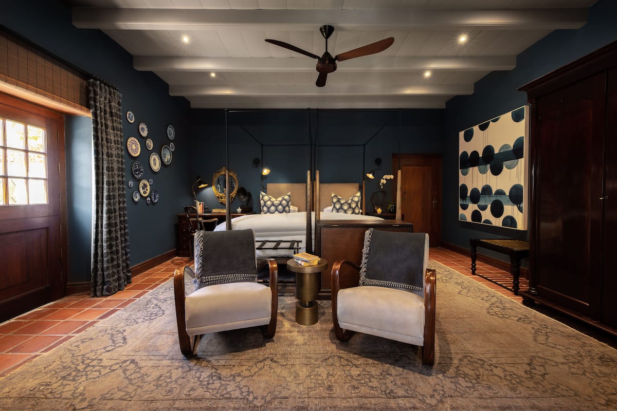 Une chambre d’hôtel avec un grand lit, deux fauteuils, un ventilateur de plafond, un tapis et des décorations murales.