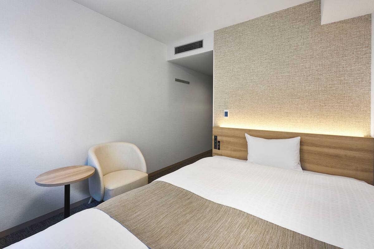 A hotel room with a bed, a chair, a small table, and a textured wall.