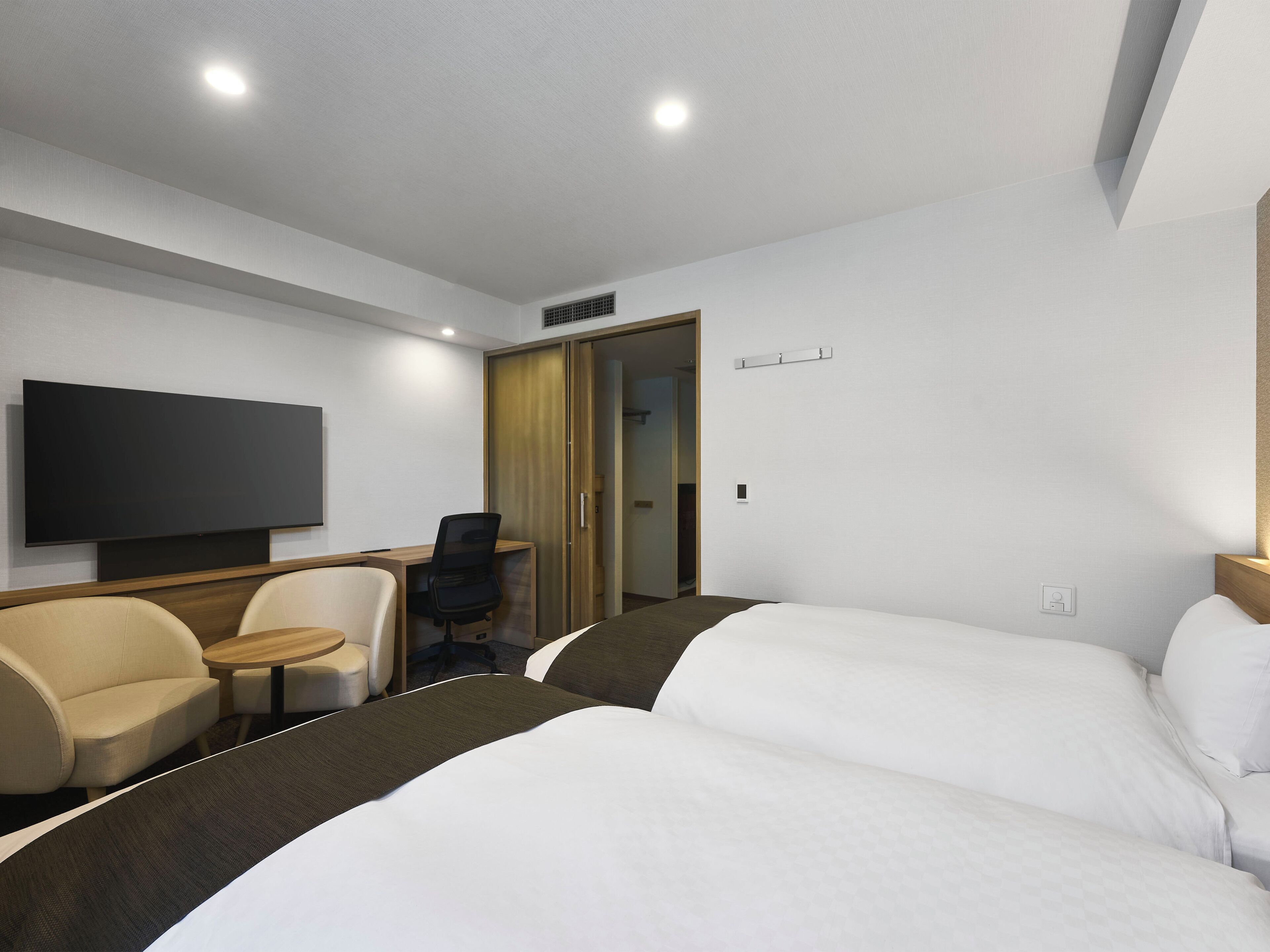 A hotel room with a bed, a desk, a chair, a television, and a wardrobe.