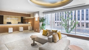 Un'area reception di un hotel dal design moderno, con scrivania, posti a sedere e ampie finestre che offrono vista sulla città.