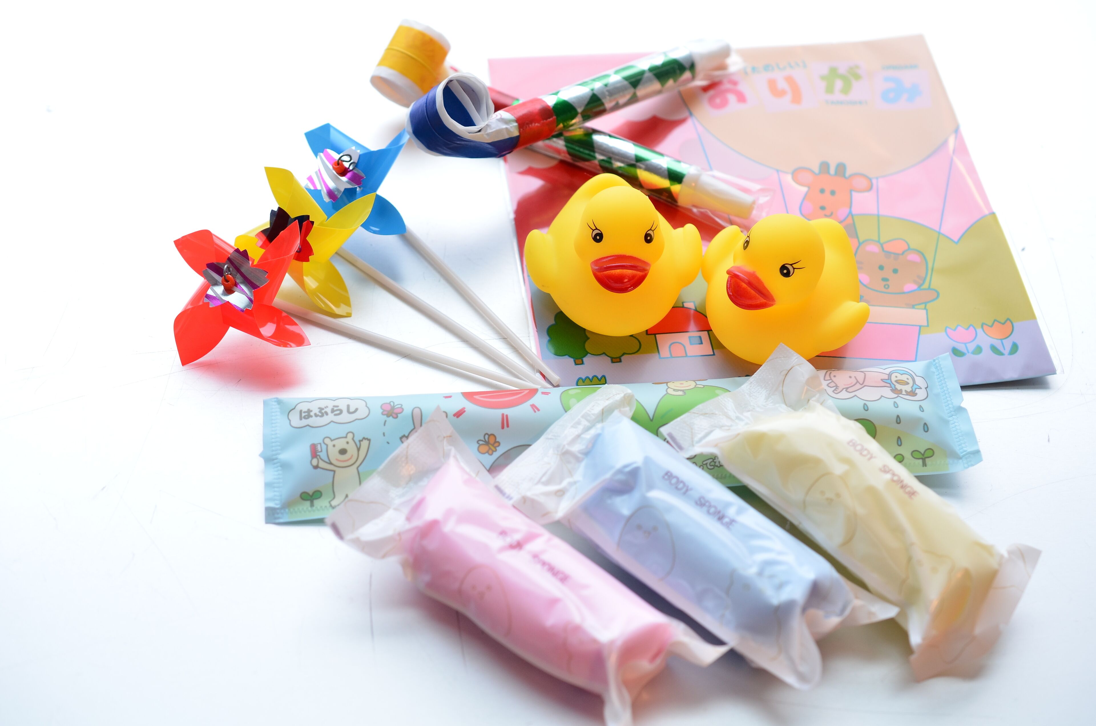 A variety of colorful stationery items including a pinwheel, rubber ducks, and packaged body sprays.