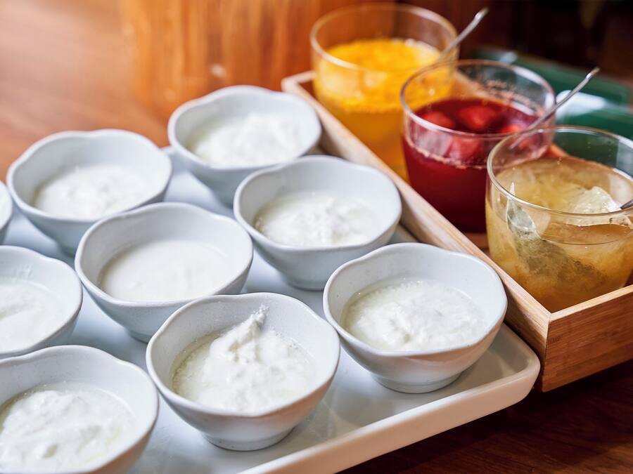 A tray with several bowls of white substance, possibly yogurt, and two glasses with iced drinks.