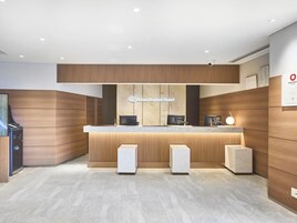 Un'area di accoglienza hotel dal design moderno, con una reception, due grandi altoparlanti e un cartello del Daiwa Roynet Hotel.