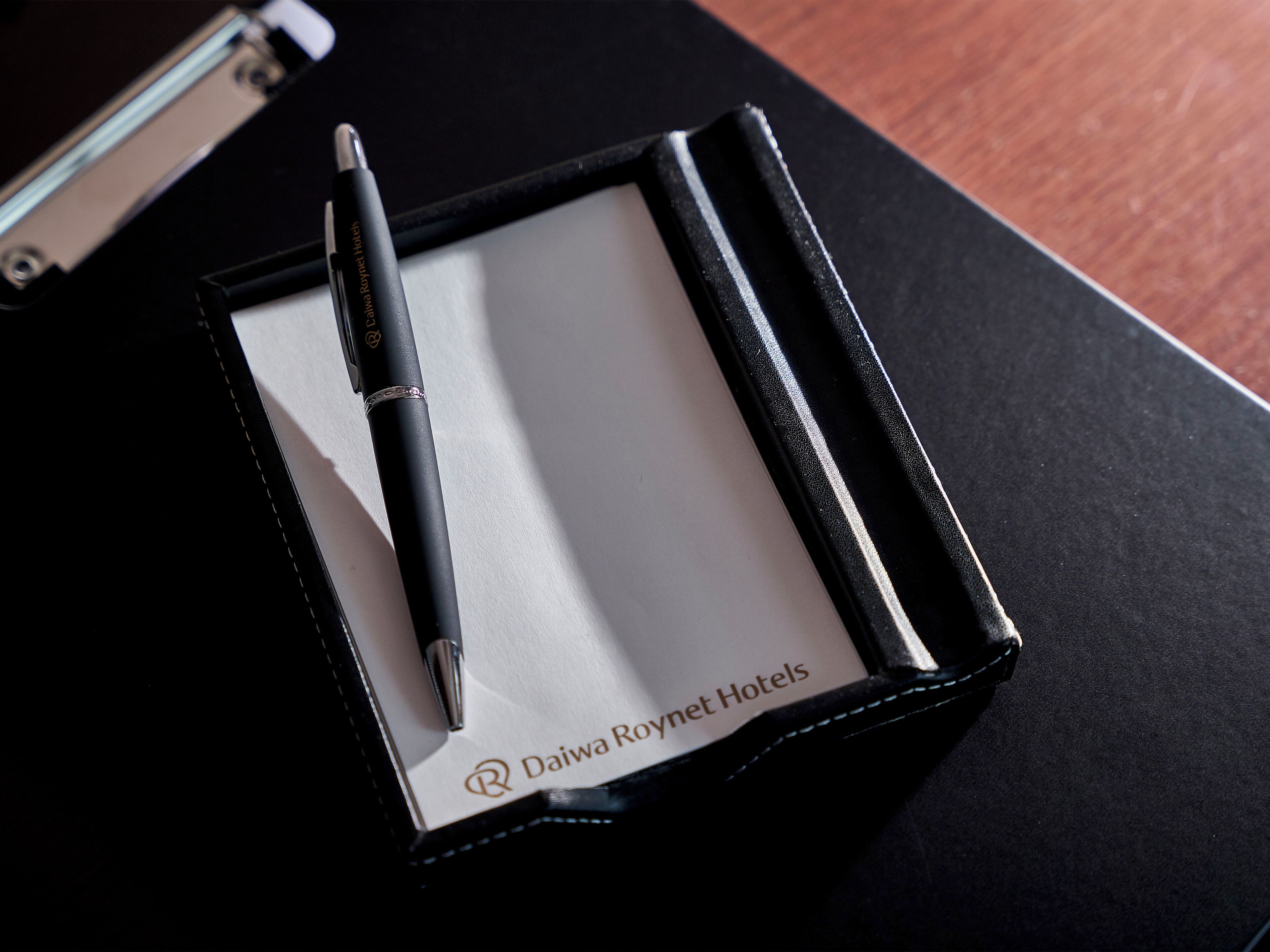 Una penna nera in una scatola nera con interno bianco, posizionata su una superficie nera con un logo che riporta la scritta "Daiwa Roynet Hotels".