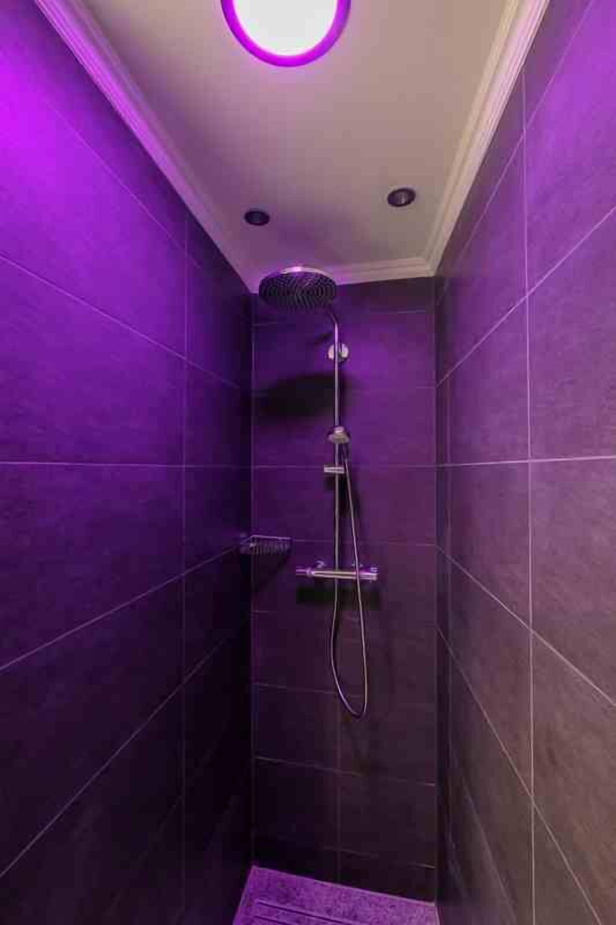 Un baño pequeño con azulejos morados, un cabezal de ducha de mano y un grifo empotrado.