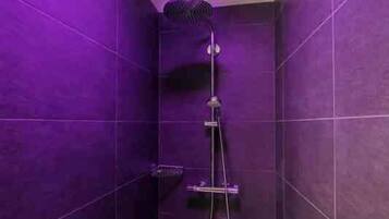 Un baño pequeño con azulejos morados, un cabezal de ducha de mano y un grifo empotrado.