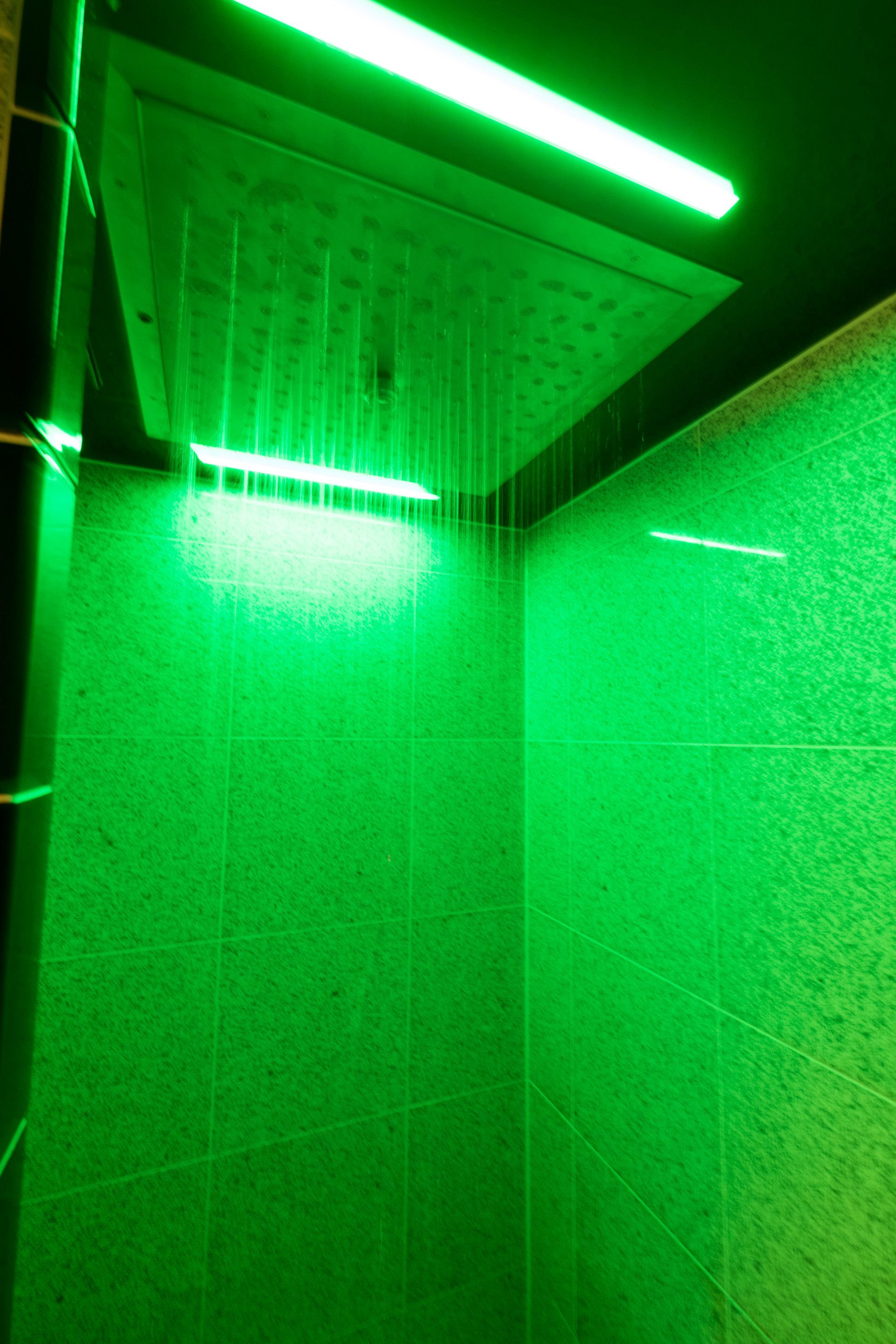 A room with a green-lit ceiling and tiled walls.