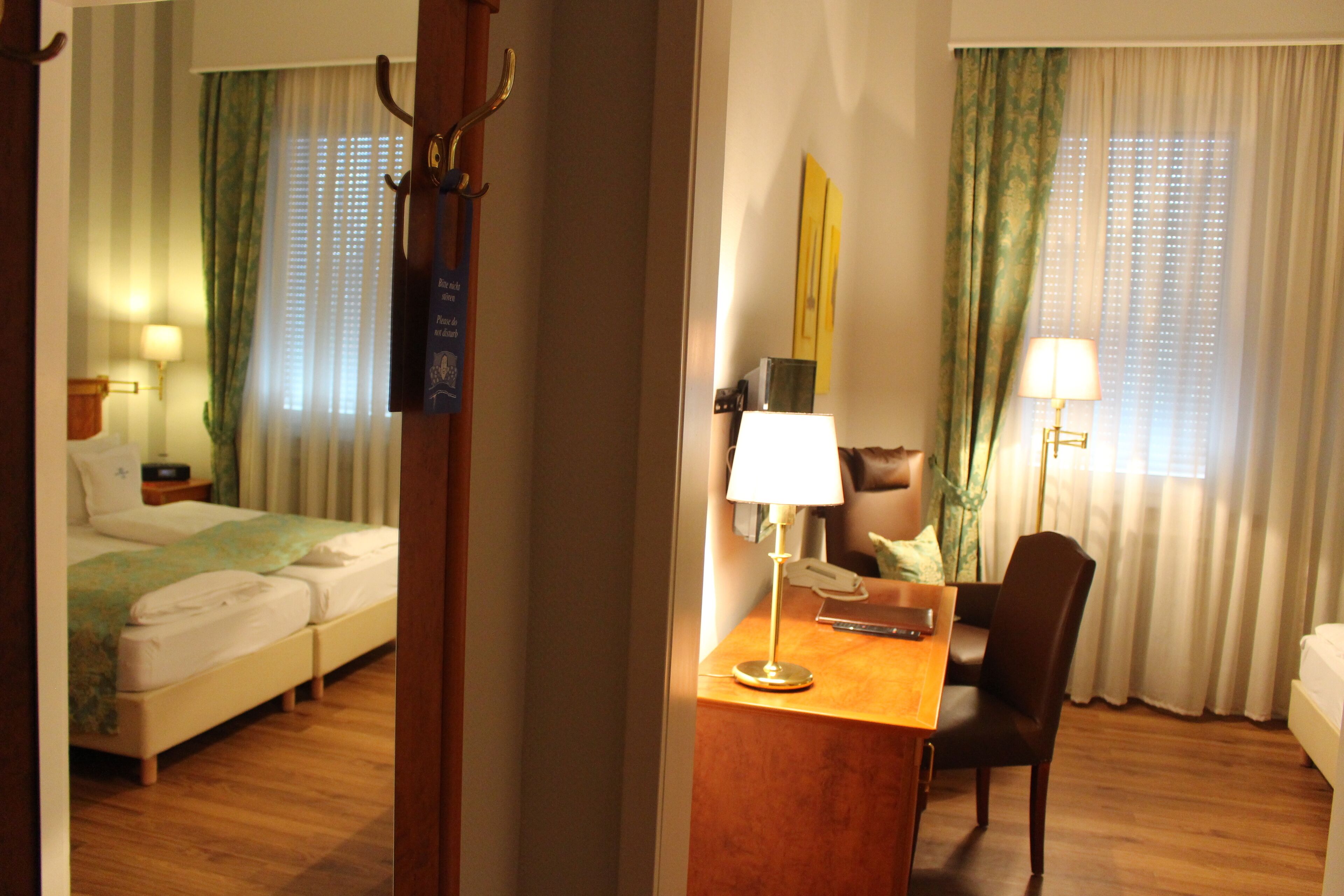 A hotel room with a bed, a desk with a lamp, a chair, and a desk lamp.