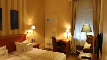 A hotel room with a bed, two bedside tables, a desk with a chair, a television, and a window with curtains.