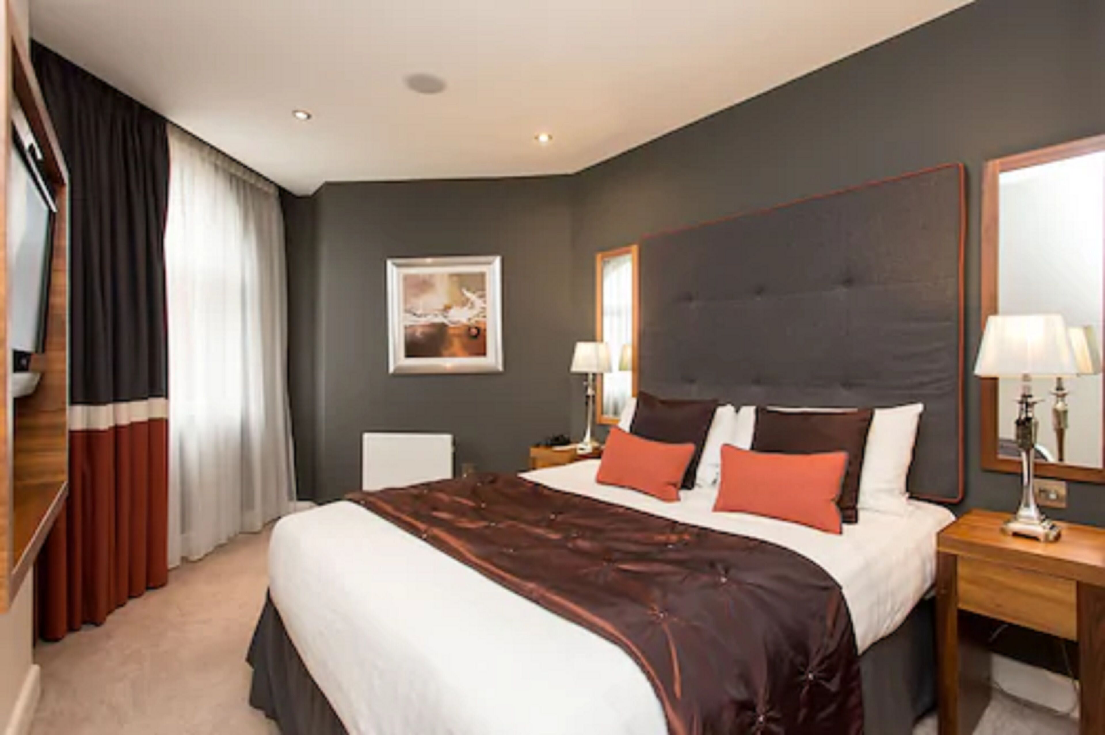 A hotel room with a large bed, a nightstand, a lamp, a mirror, and a framed picture on the wall.