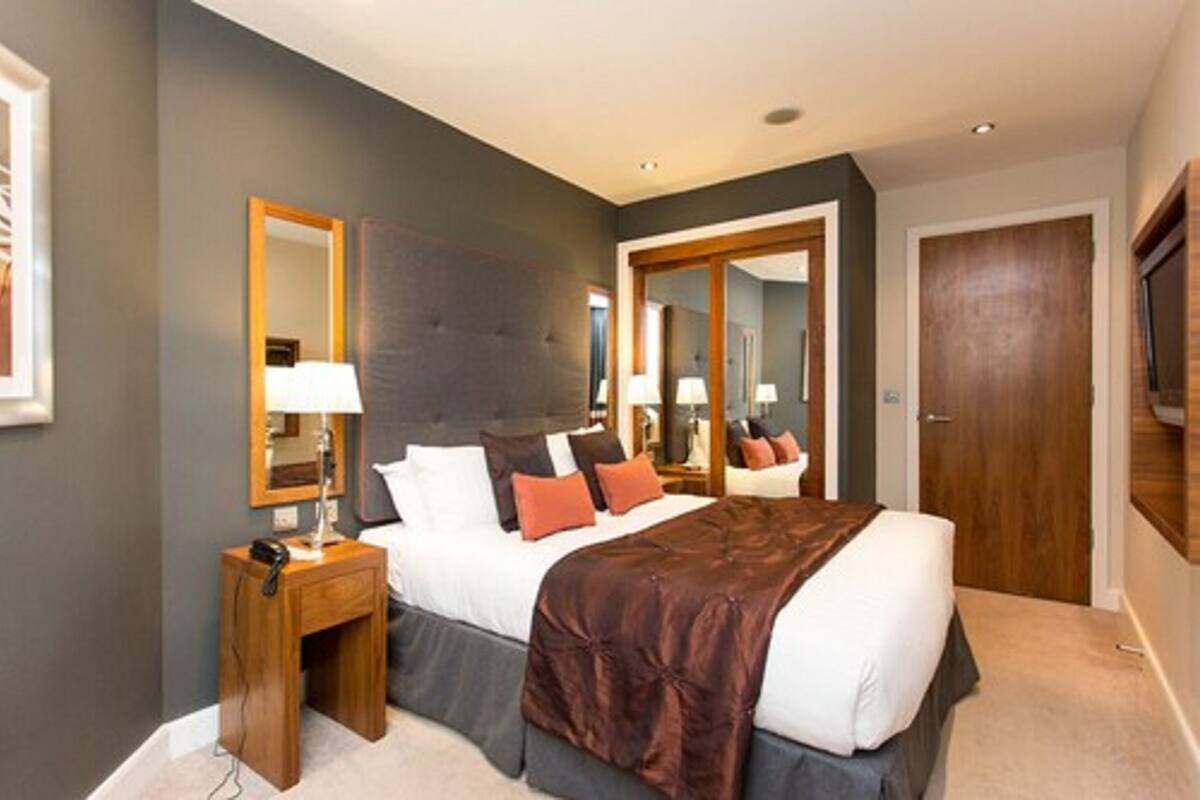 A modern hotel room with a large bed, bedside tables, a mirror, and a wardrobe.