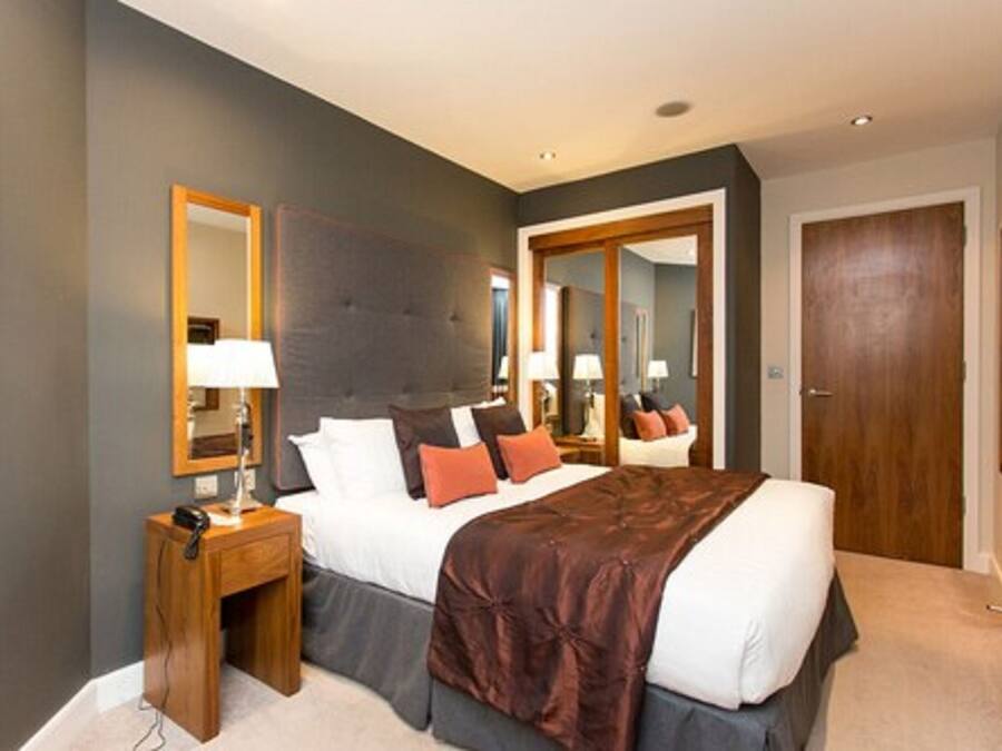 A modern hotel room with a large bed, bedside tables, a mirror, and a wardrobe.