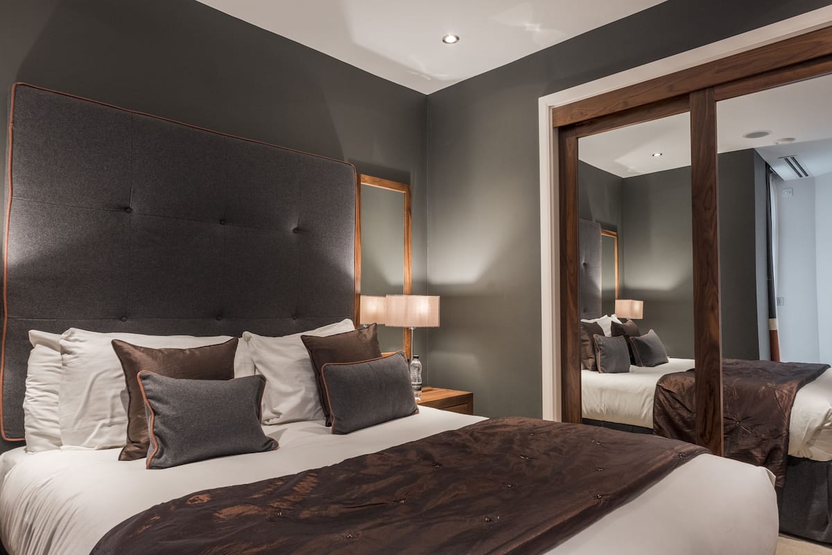 A modern hotel room with a large bed, a wooden headboard, and a large mirror.