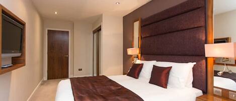 A hotel room with a large bed, a wooden headboard, a bedside table with a lamp, and a mirror.