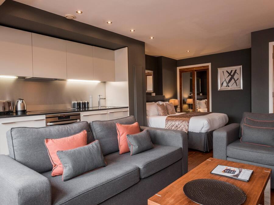 A modern living room with a grey sofa, a wooden coffee table, and a kitchen in the background.