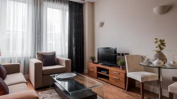 A modern living room with a sofa, a glass coffee table, a TV, and a dining area with a glass table and chairs.