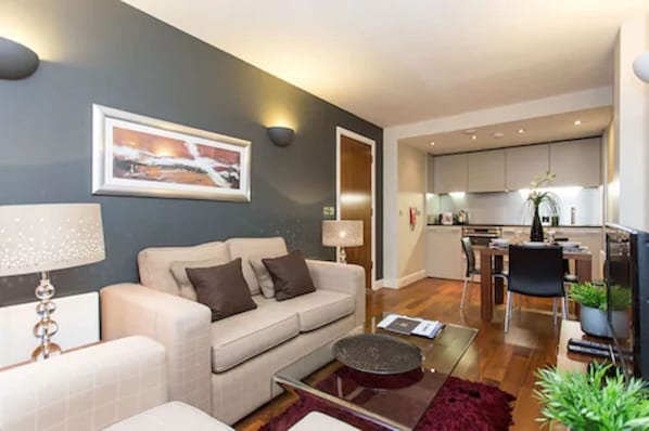 A modern living room with a sofa, coffee table, and a dining area with chairs. - The Chambers - Park Place - Apartments (Leeds)