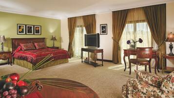 Quarto de hotel com cama, televisão, escrivaninha, cadeira e sofá floral.