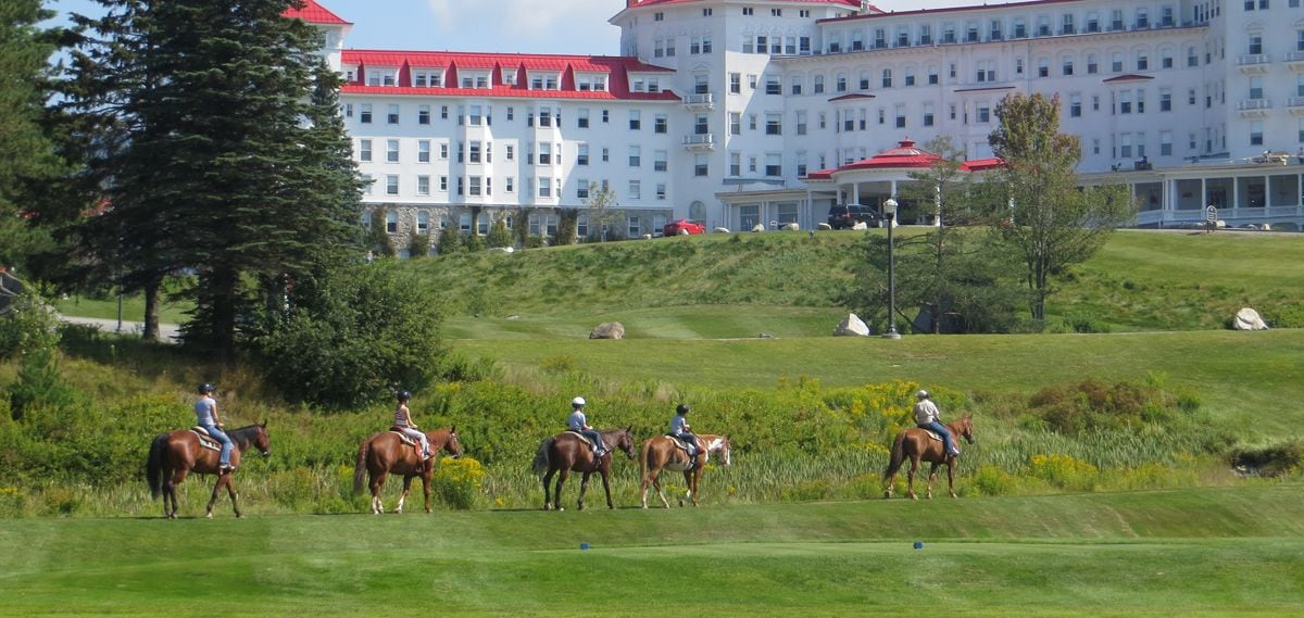 A group of people riding horses on a grassy area with a large building in the background.