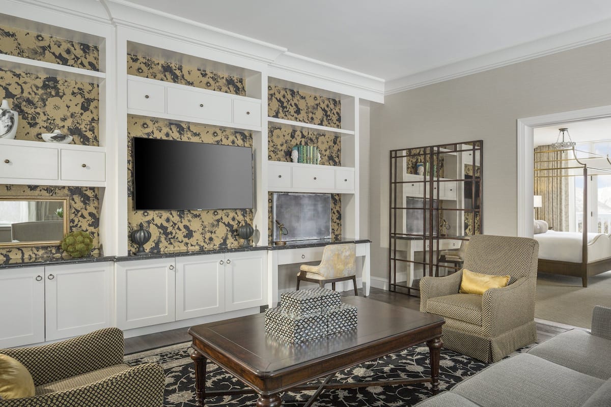 Een woonkamer met een bank, fauteuils, een salontafel, een flatscreen televisie en ingebouwde planken met decoratieve objecten.