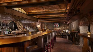 A bar area with a brick floor, wooden bar counter, and leather bar stools.