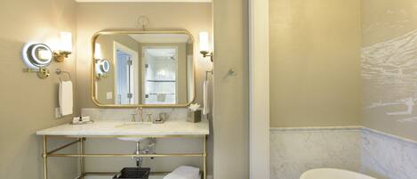 Une salle de bain avec une coiffeuse dotée d’un cadre doré, un grand miroir et une baignoire.
