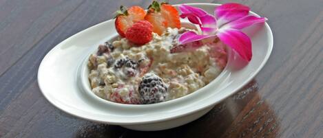 Un bol de porridge aux fraises, avec une fleur rose, posé sur une table en bois.