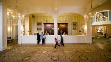A grand lobby with a reception desk, chandeliers, and a patterned carpet.