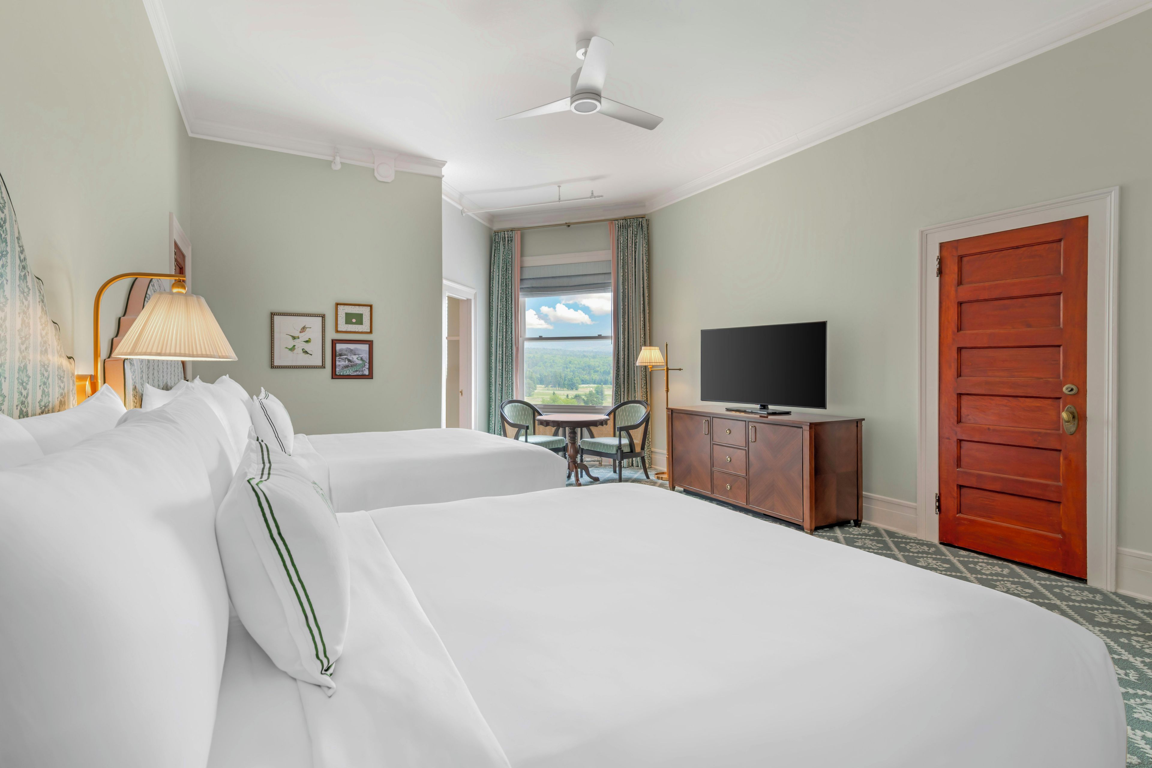 Camera d'albergo con due letti, televisione, una scrivania con sedia e vista sull'esterno.