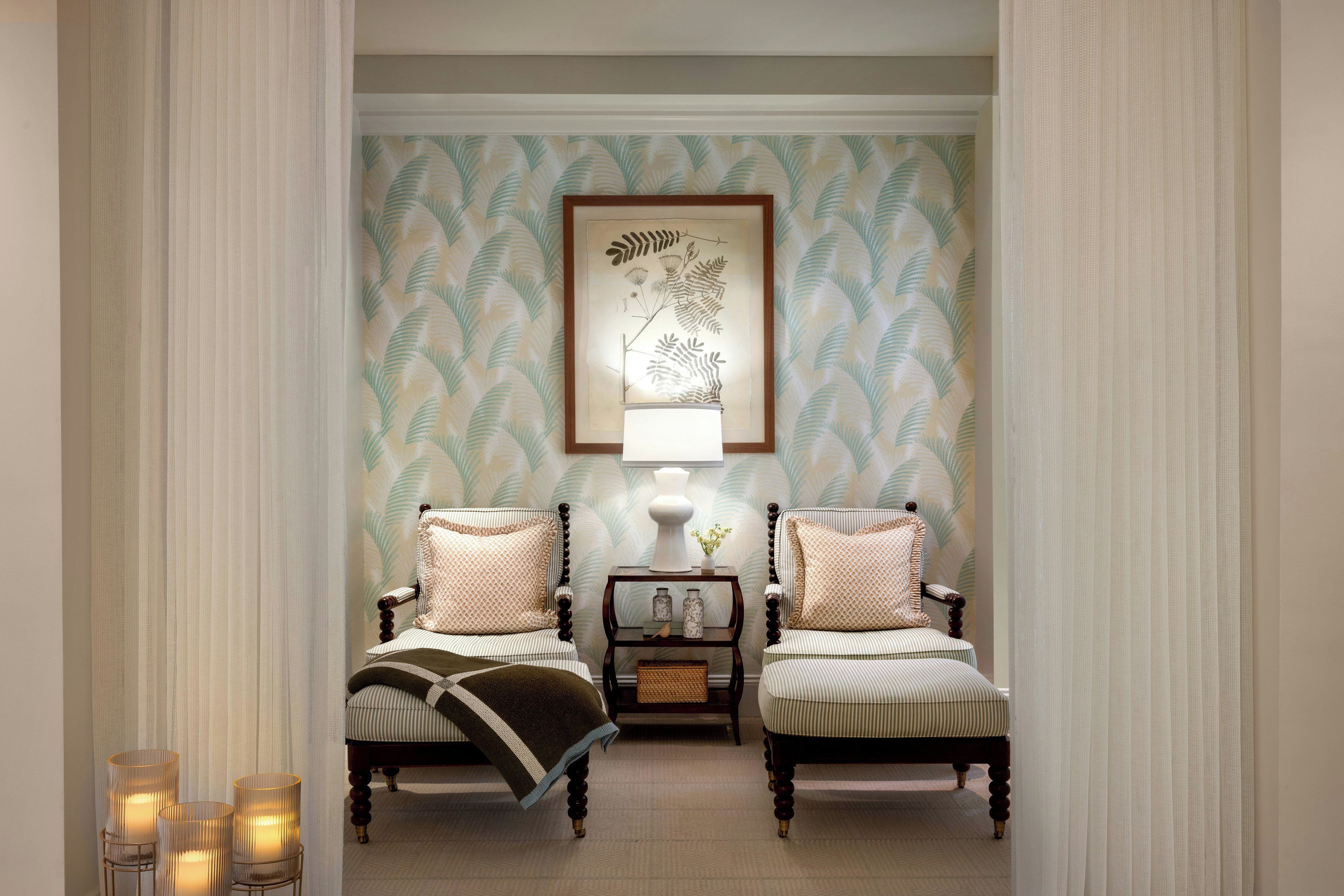 A room with two upholstered chairs, a small table with a lamp, and a framed botanical artwork on the wall.
