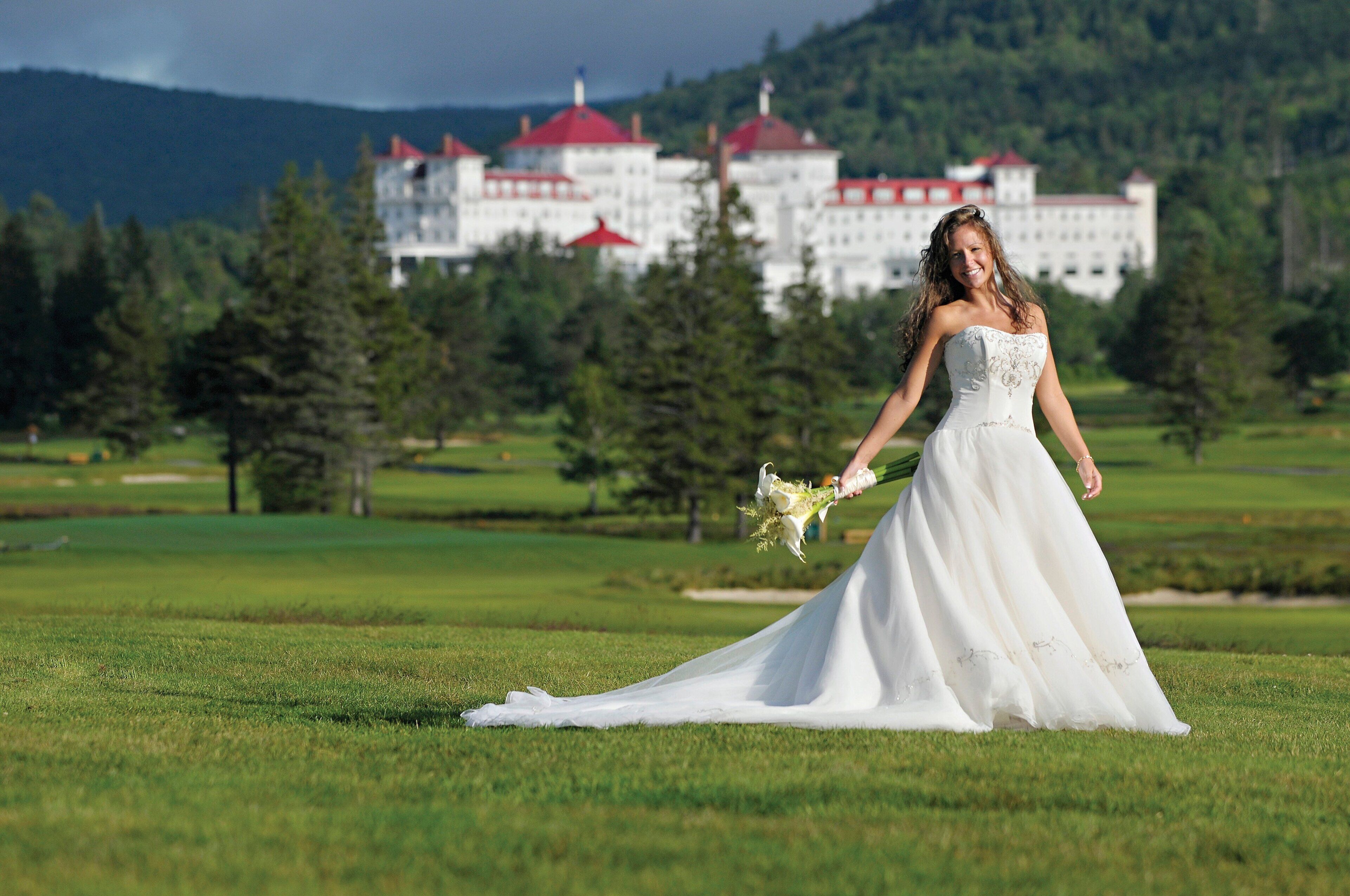 A wedding dress on a grassy field with a building in the background.