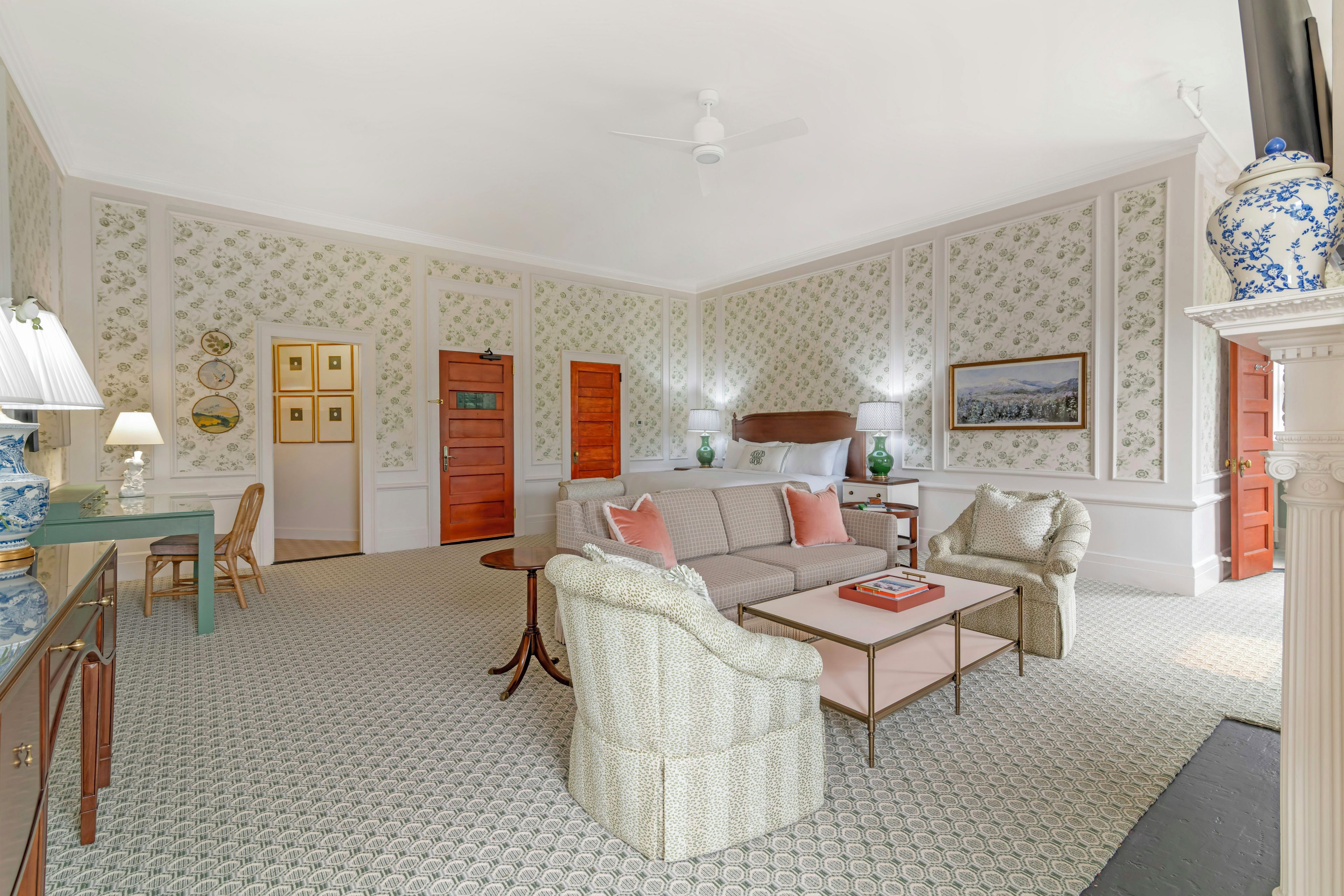 A room with a bed, two chairs, a coffee table, a desk, and a fireplace.