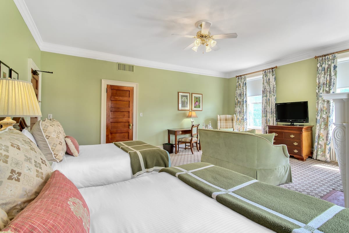 A hotel room with two beds, a television, a dresser, and a ceiling fan.