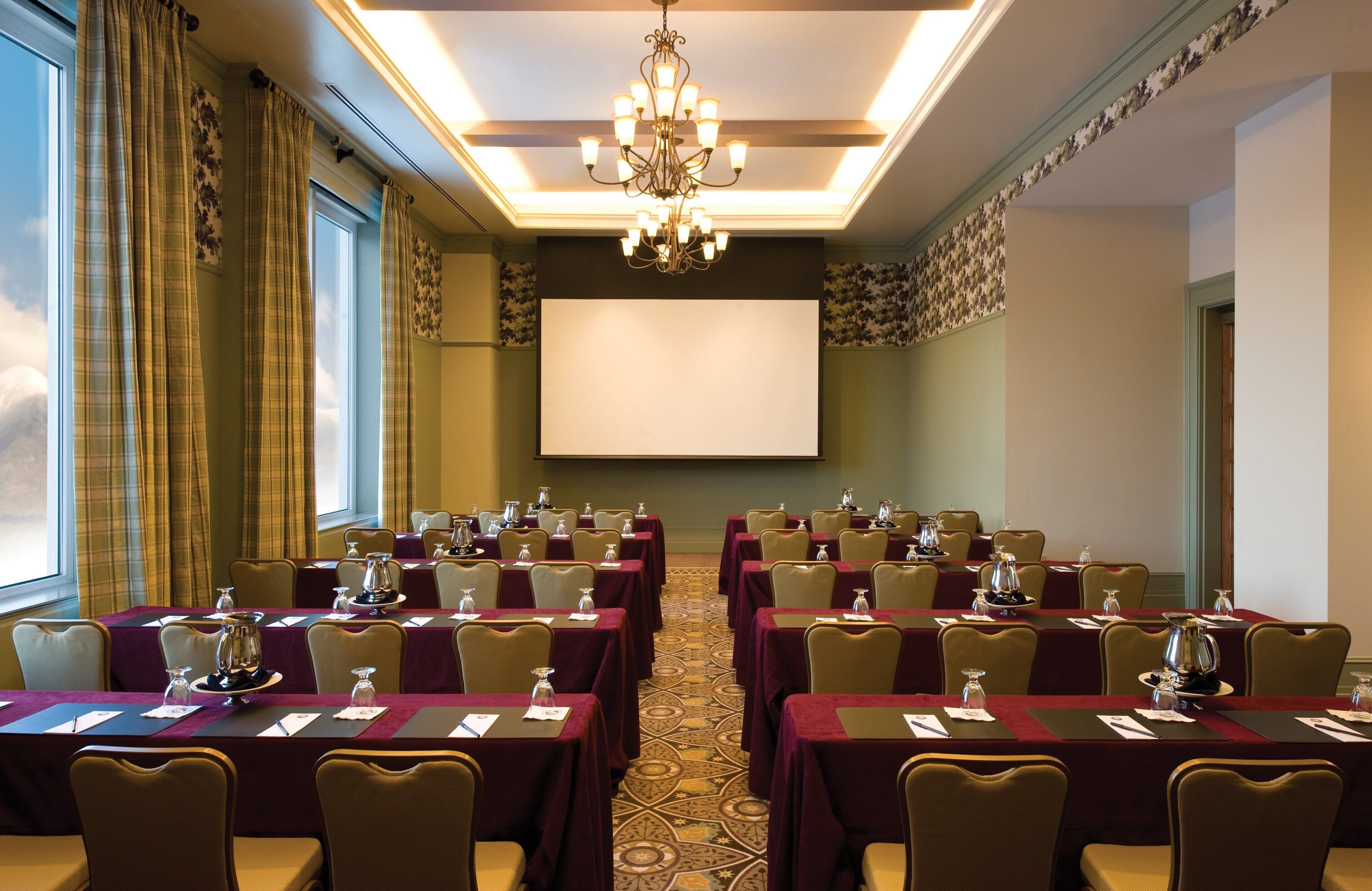 A conference room with tables, chairs, a projector screen, and a chandelier.