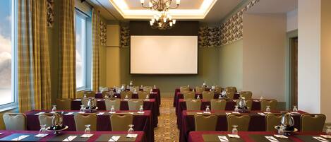 A conference room with tables, chairs, a projector screen, and a chandelier.