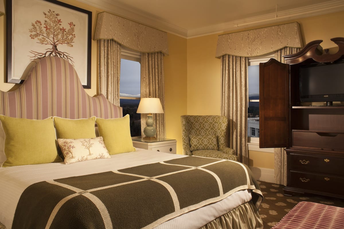 A hotel room with a large bed, a television, a chair, and a dresser.