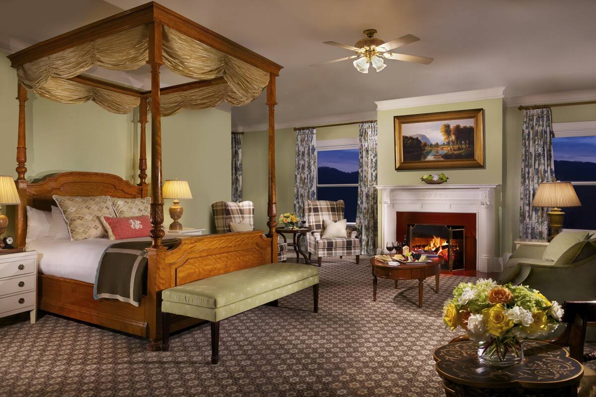 A four-poster bed with a canopy, a fireplace, a painting, and a view of the outdoors.