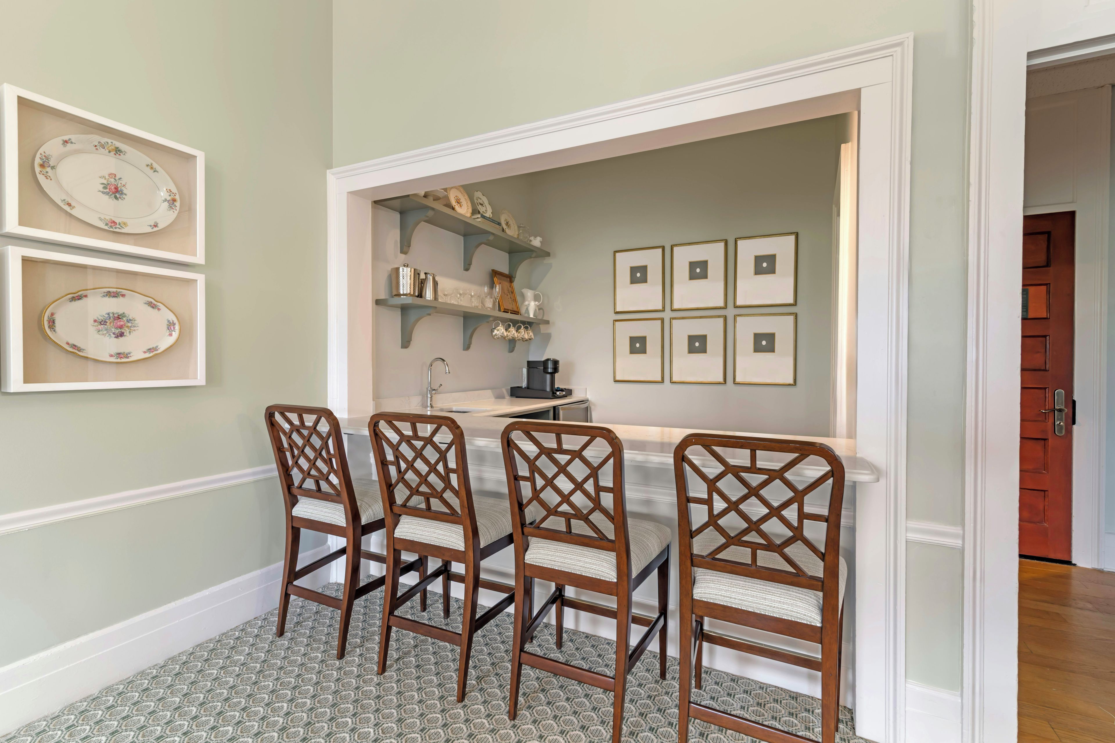 A dining area with a white table, four wooden chairs, and a patterned rug.