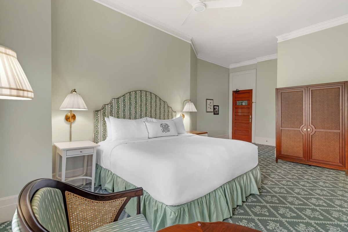 Une chambre à coucher bien rangée, avec un grand lit, des lampes de chevet, une armoire en bois et une chaise.